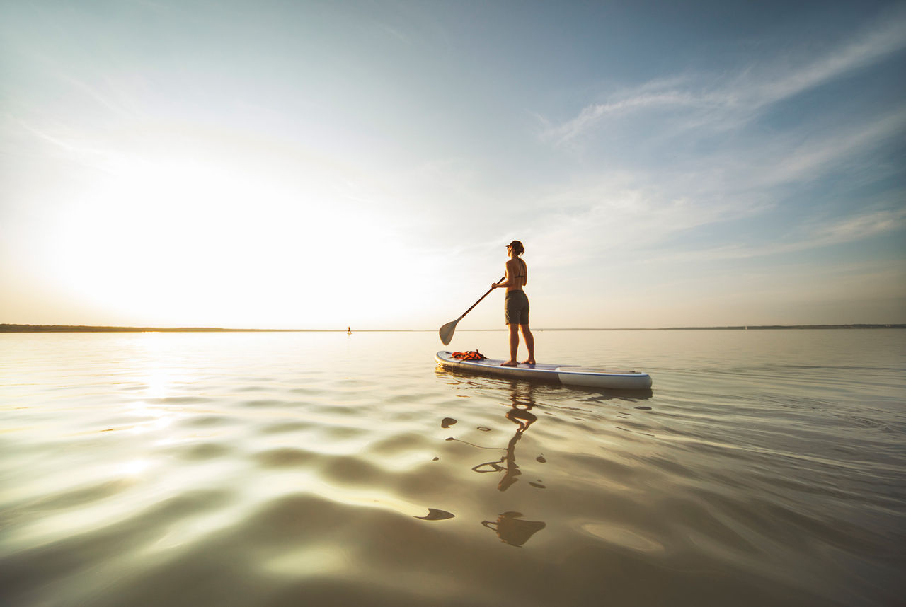 Woman balancing on a canoe in water and facing towards the sky.