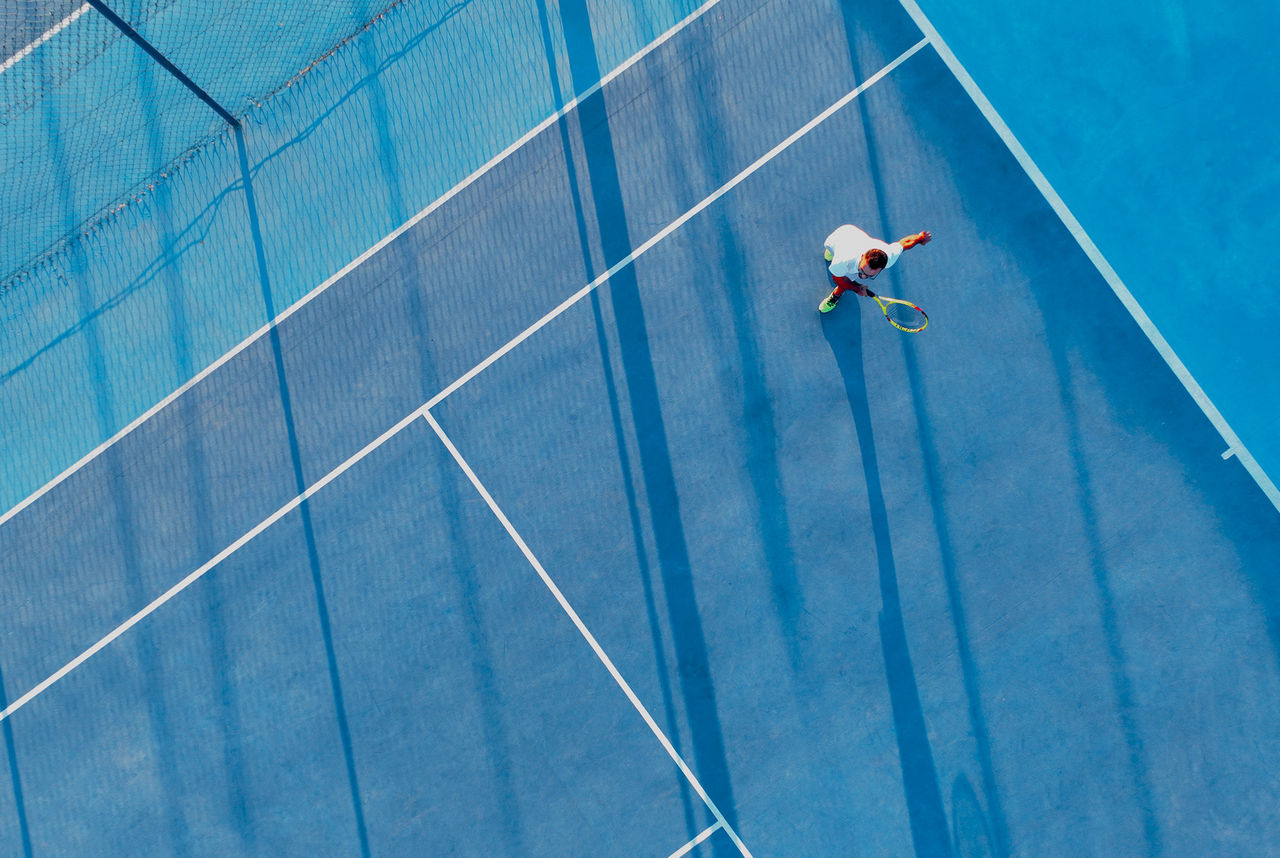 Directly above view of a tennis player on a blue tennis court.